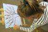 Na zdjęciu dziewczynka ozdabia drzewo namalowane na kartce papieru.