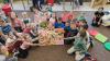 Grupa dzieci siedząca na dywanie z największą książką w oddziale dla dzieci.