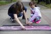 Dziewczynka maluje cytat na chodniku z pomocą dorosłej kobiety.