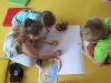 Na zdjęciu grupka dzieci malująca na kartkach papieru. 