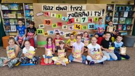 Na zdjęciu dzieci siedzące przed planszą z hasłem "Raz, dwa, trzy... zaGRAJ i TY".