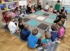 Dzieci siedzą wraz z bibliotekarką na dywanie i rozmawiają.