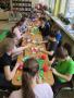 Na zdjęciu grupka dzieci siedząca przy stolikach i wykonująca prace plastyczne. 